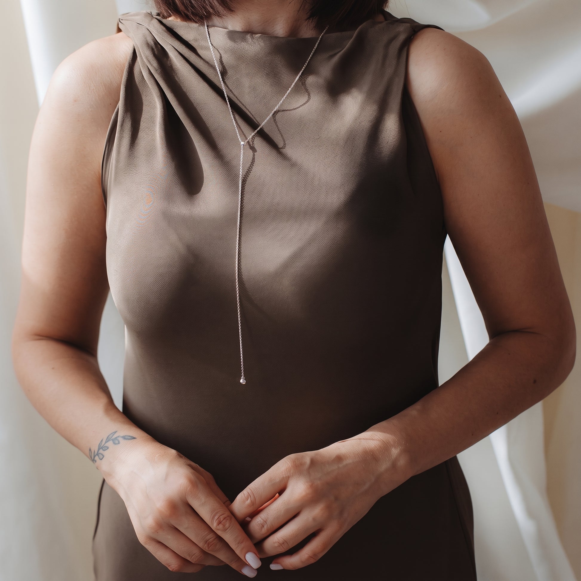 Close-up of a person wearing a sterling silver bola (lariat) necklace over a taupe satin dress in soft indoor light.