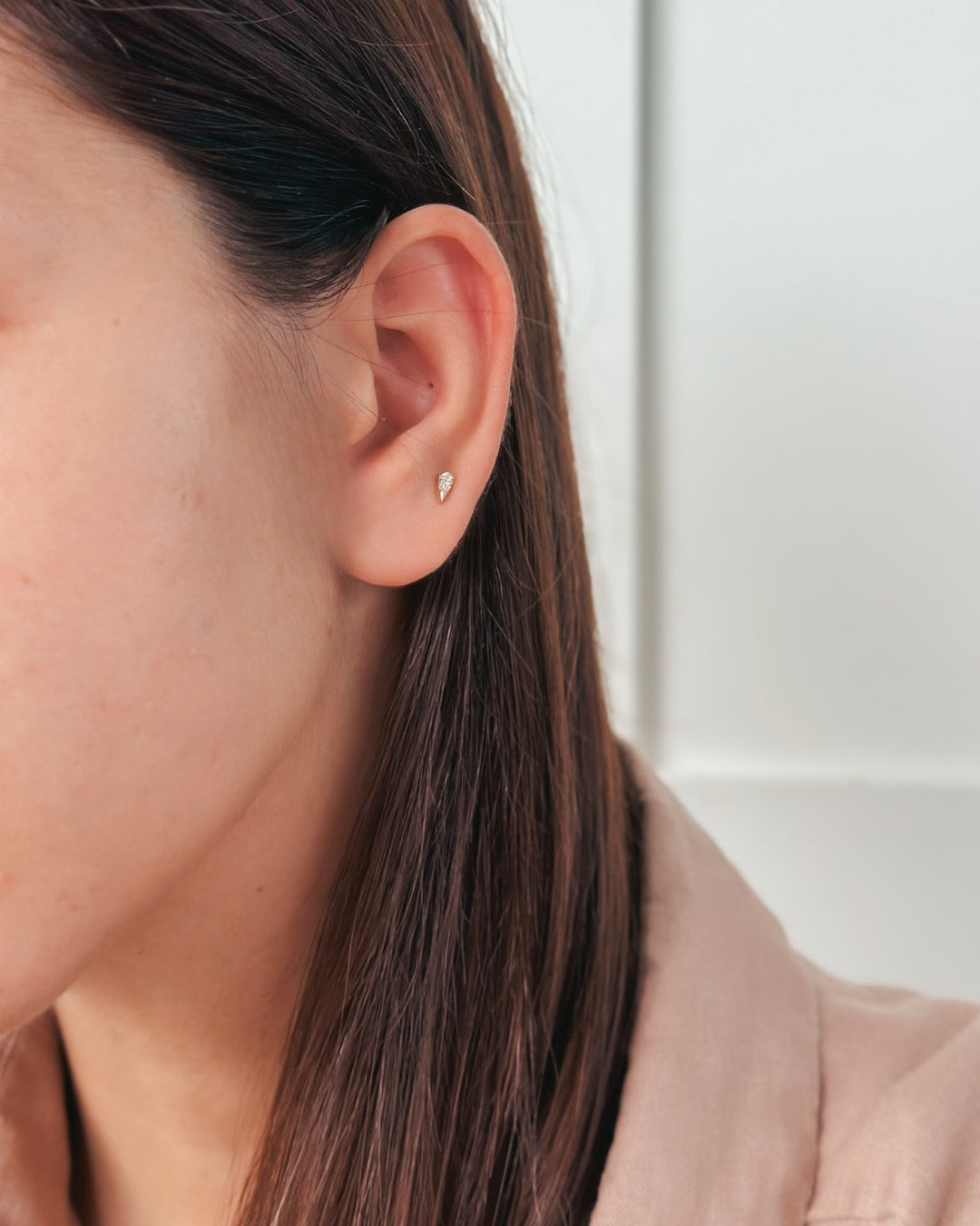 Close-up of a person's ear featuring a small earring against a light background.