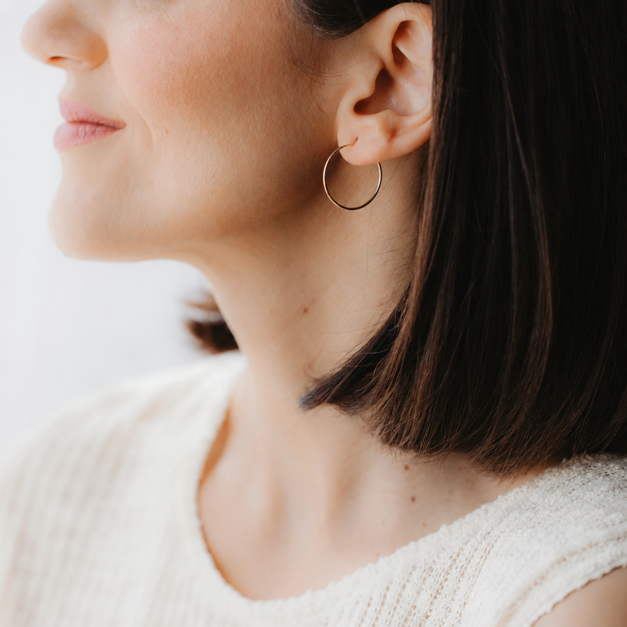 Close-up of a model’s ear wearing a mini 14K yellow gold hoop earring in soft natural light.