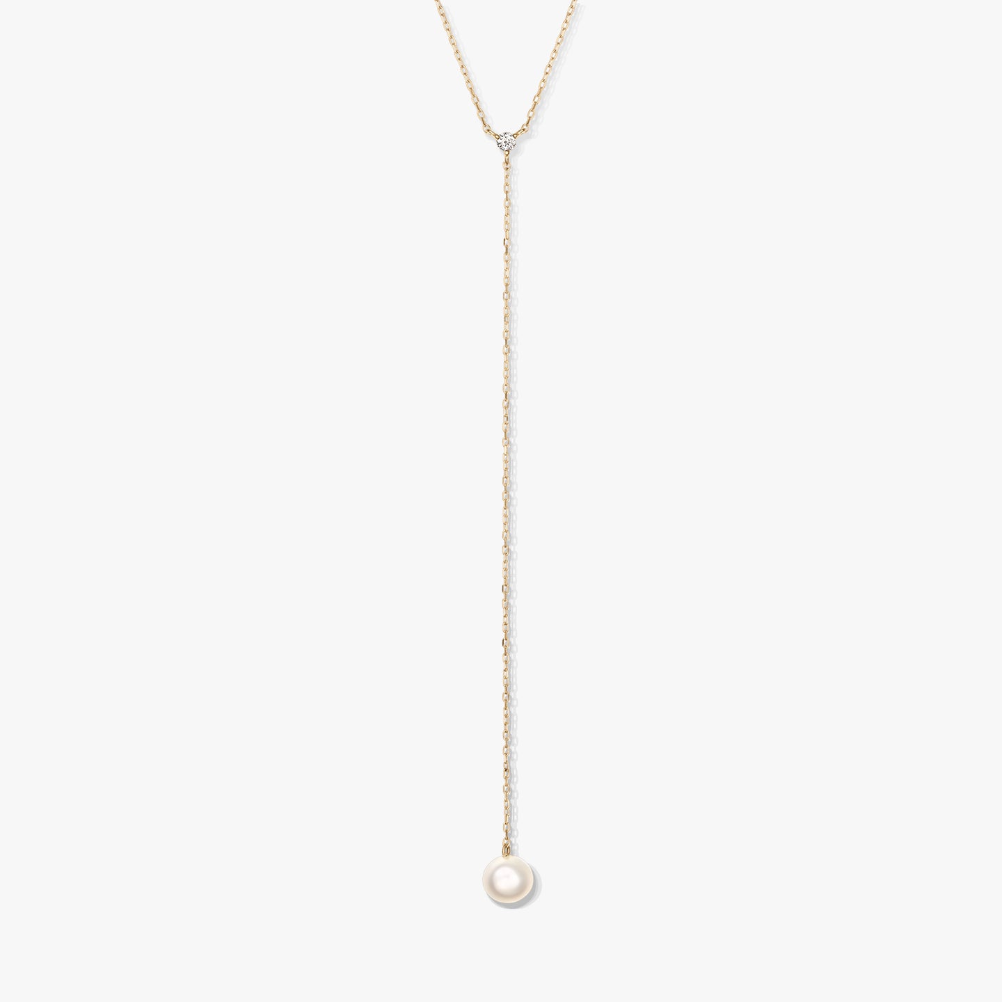 Minimalist gold lariat necklace featuring a single round white pearl drop and a delicate accent stone, centered on a white background.