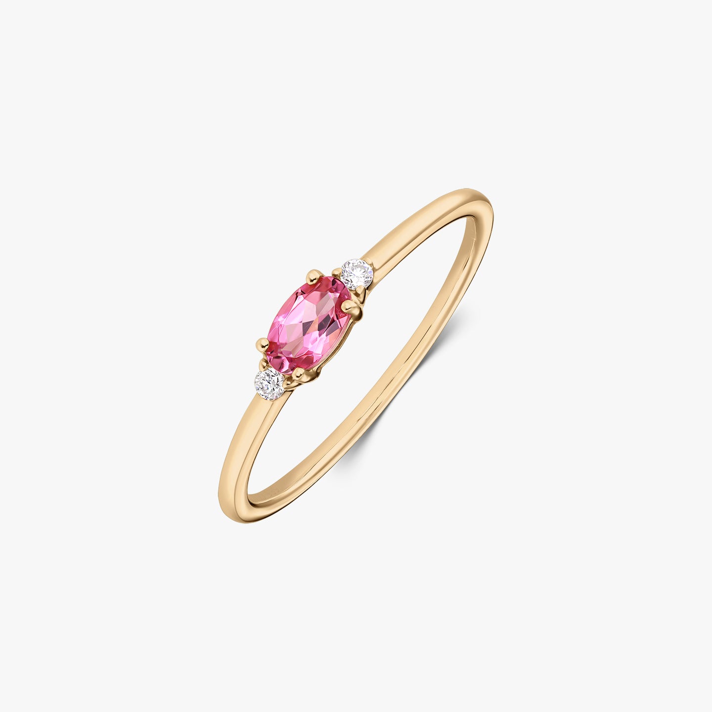 14K yellow gold ring with an oval pink tourmaline center flanked by two small round diamonds on a slim band, isolated on white.