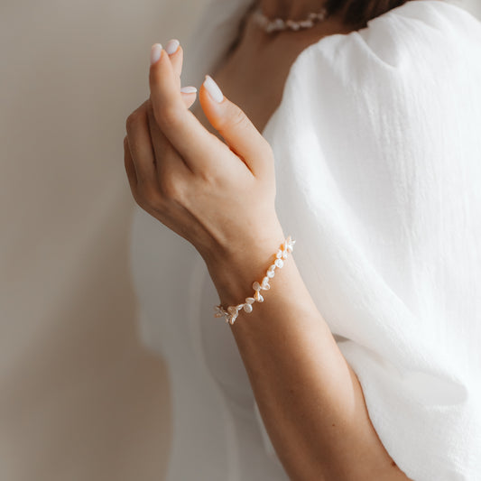 Close-up of a wrist adorned with a gold-plated sterling silver bracelet featuring pink keshi pearls, styled with a white puff-sleeve top.
