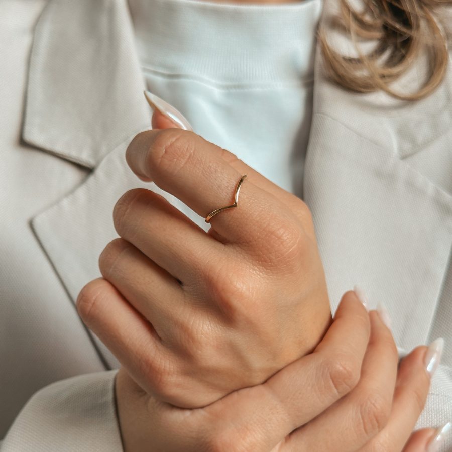 A person adorned with a minimalist V-shaped gold ring on their finger, dressed in a light-colored suit.