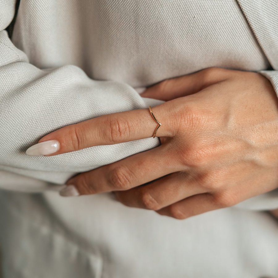 Close-up of a hand wearing a minimalist gold-plated silver ring against a light fabric background.
