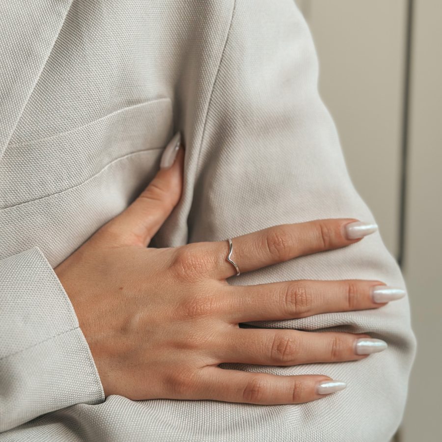 Close-up of a hand wearing a Simple V Silver Ring on a neutral fabric background.