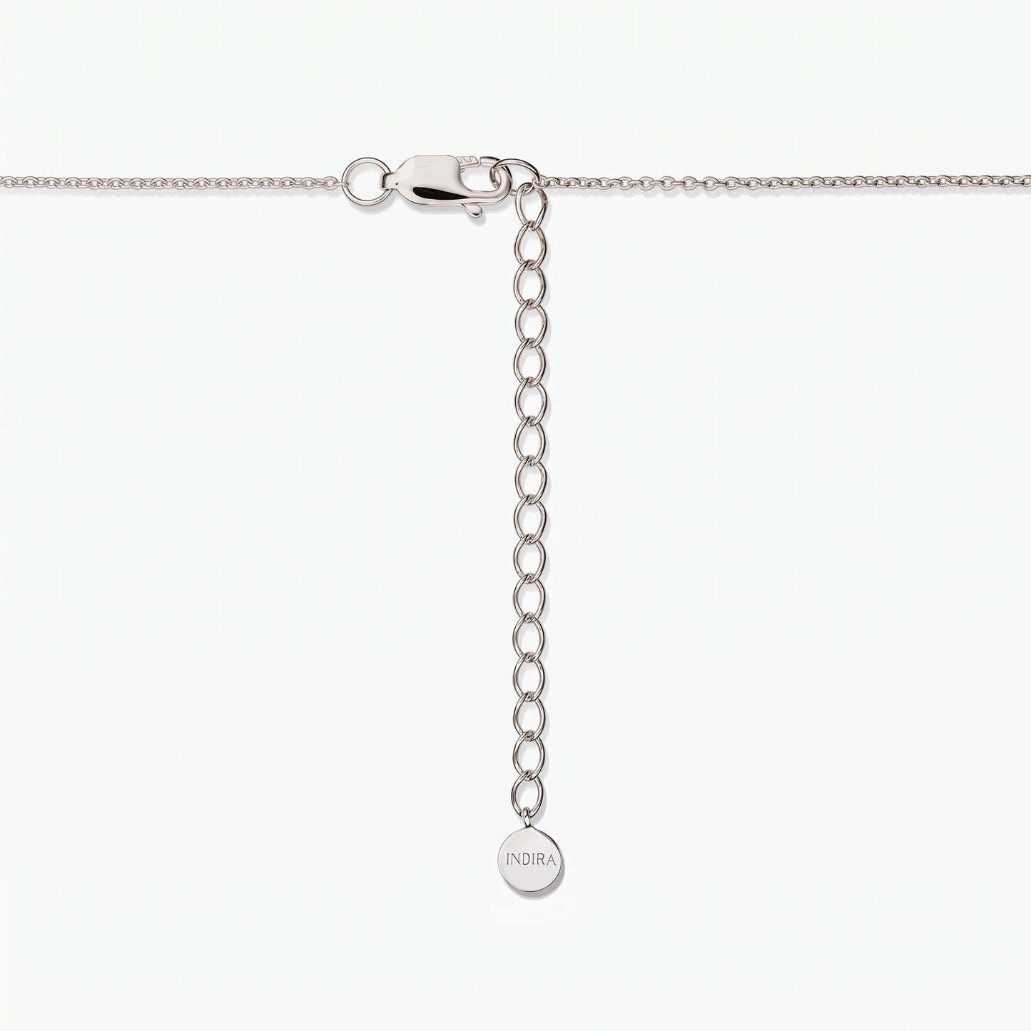 Close-up of a sterling silver necklace clasp with an adjustable extender chain and a small round tag engraved “INDIRA,” against a white background.