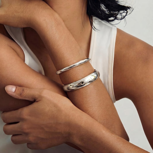 A person wearing two silver bangles on their arm, set against a neutral background.