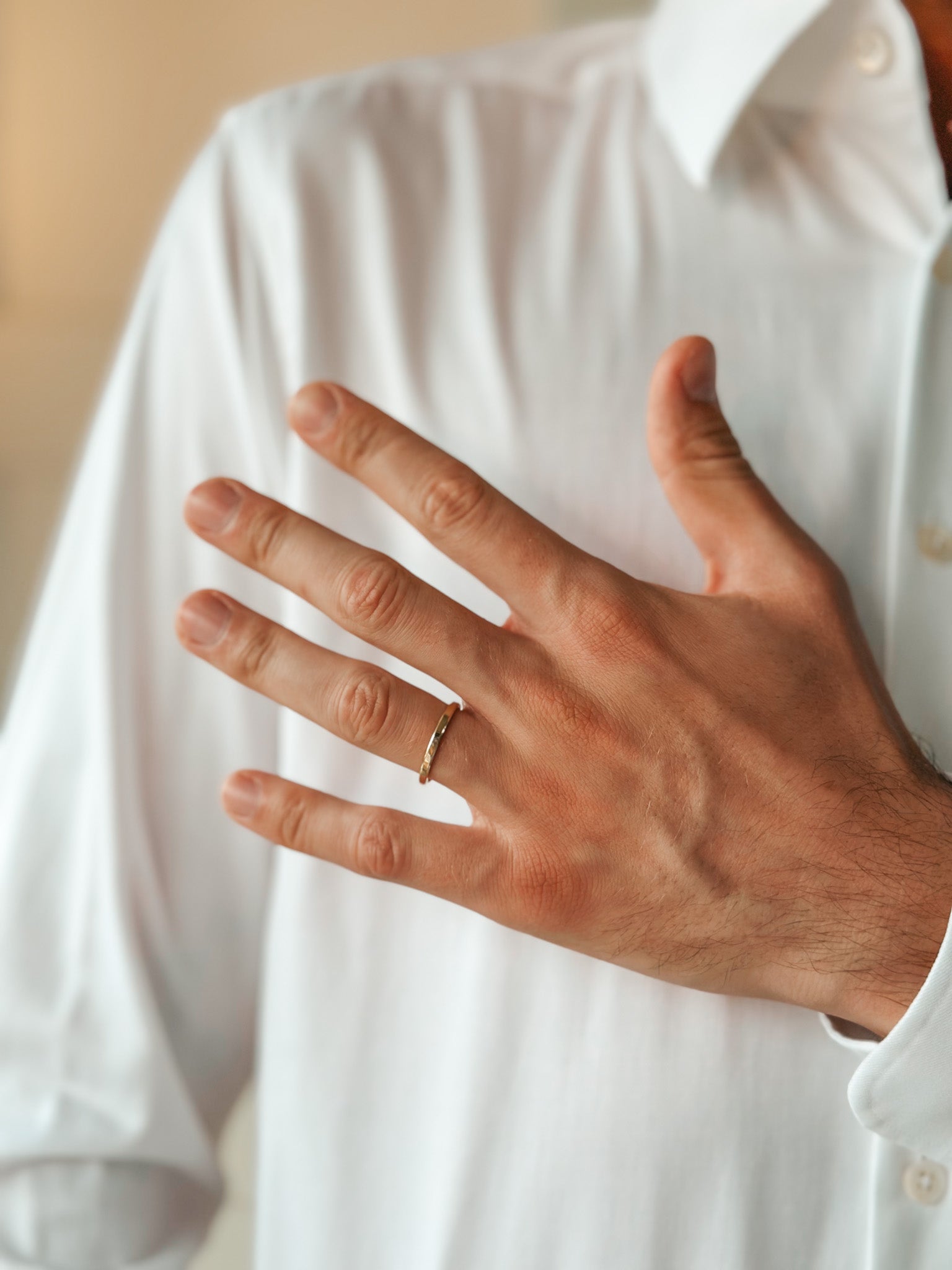 A hand adorned with a gold wedding ring on the ring finger, resting against a white shirt.