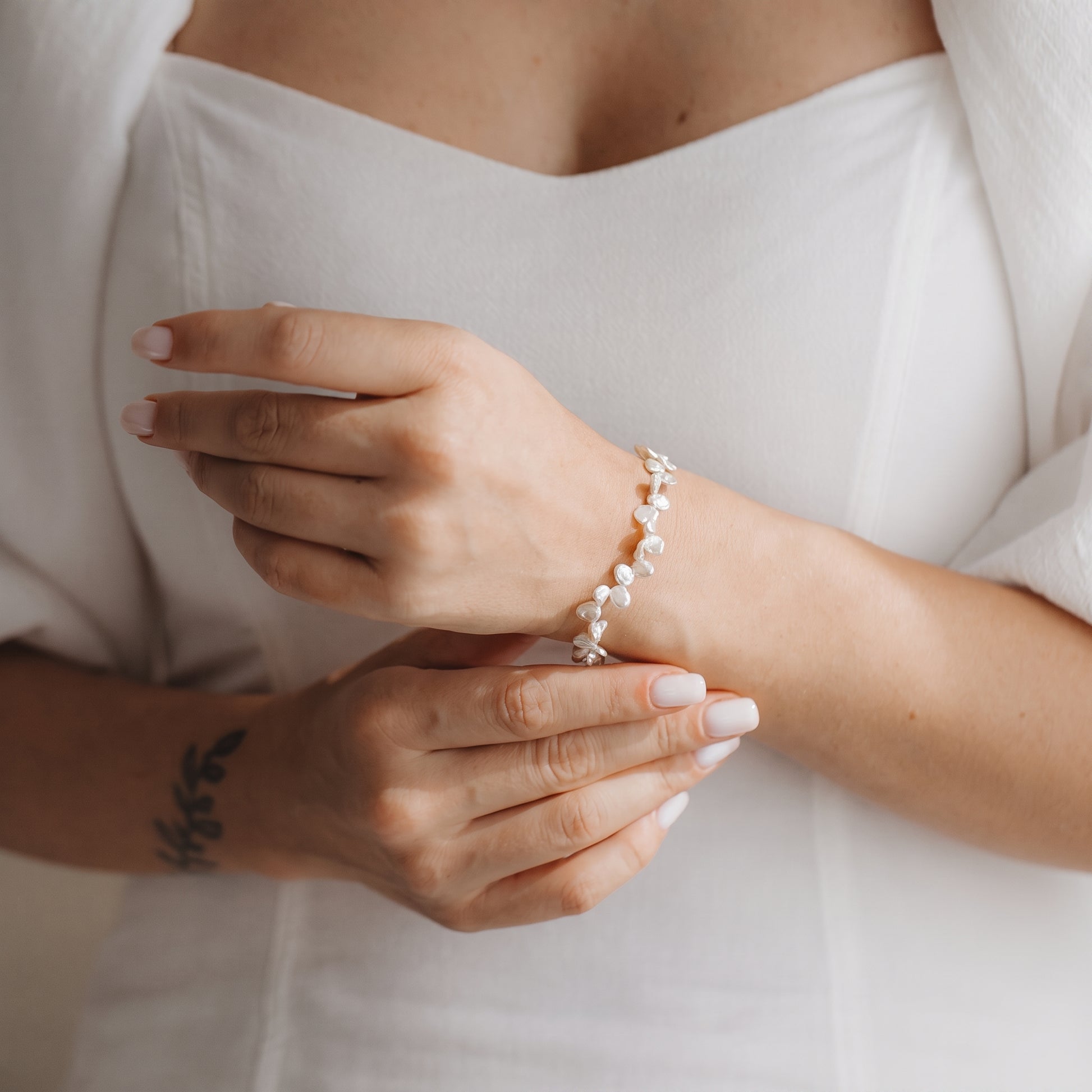 Close-up of hands wearing a gold-plated sterling silver bracelet with white keshi pearls against a white dress.