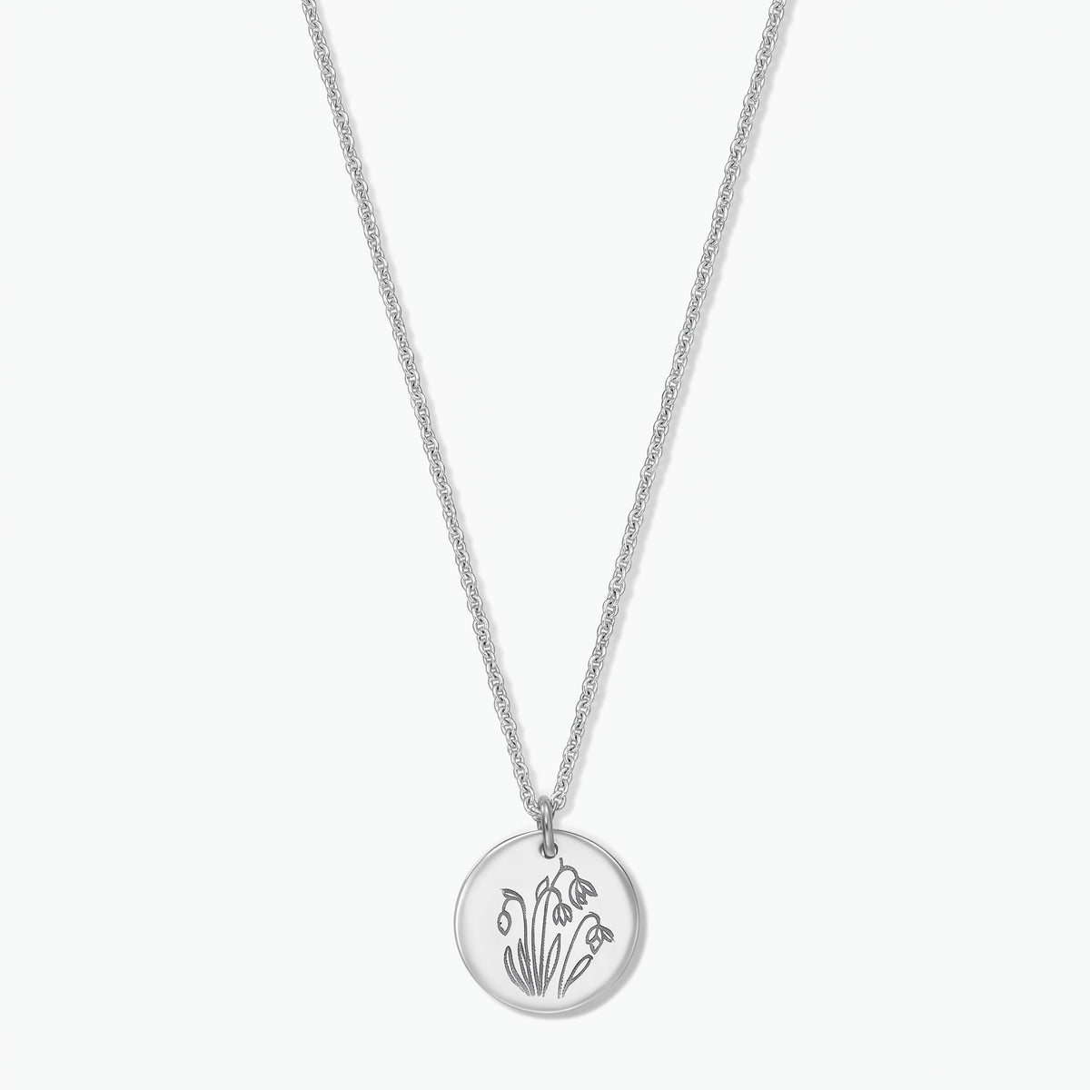 Sterling silver birth flower necklace with a round disc pendant engraved with January snowdrops on a fine chain, isolated on a white background.