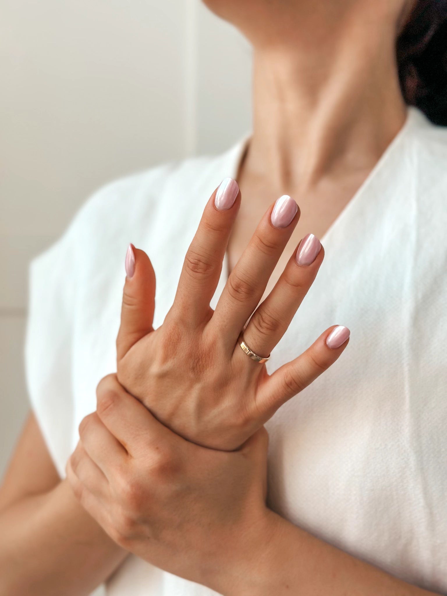 Close-up of a woman's hands with pink nail polish, wearing a gold wedding band against a light background.