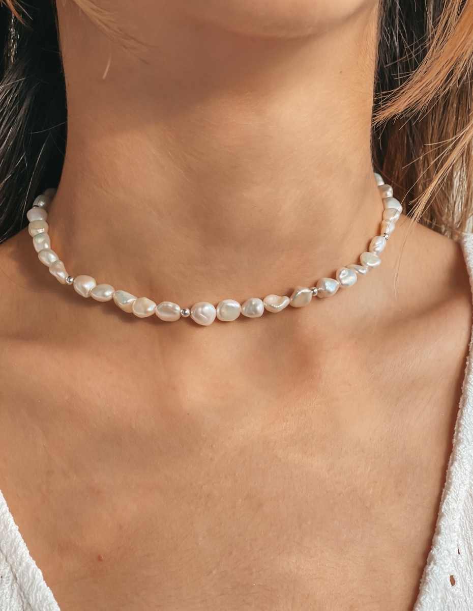 Close-up of a person's neck wearing a silver necklace with natural pearls.