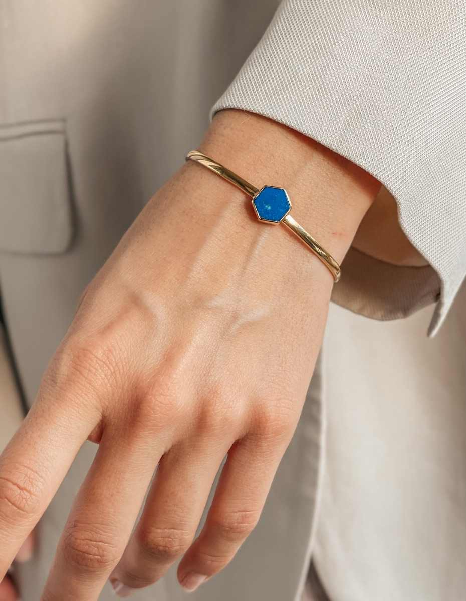 A close-up of a wrist adorned with a gold bracelet featuring a blue hexagonal stone.