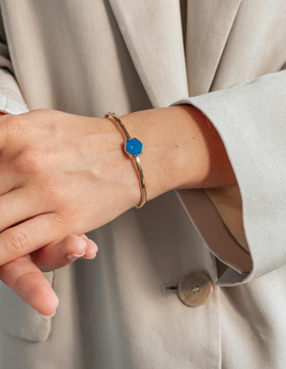 A hand wearing a silver bracelet with a blue lapis lazuli stone, against a light beige clothing background.