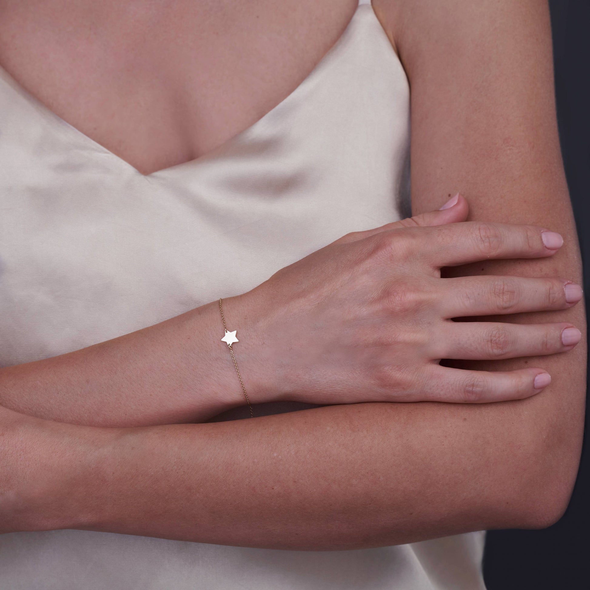 A woman's arm adorned with a delicate 14K gold star bracelet against a light-colored satin top.