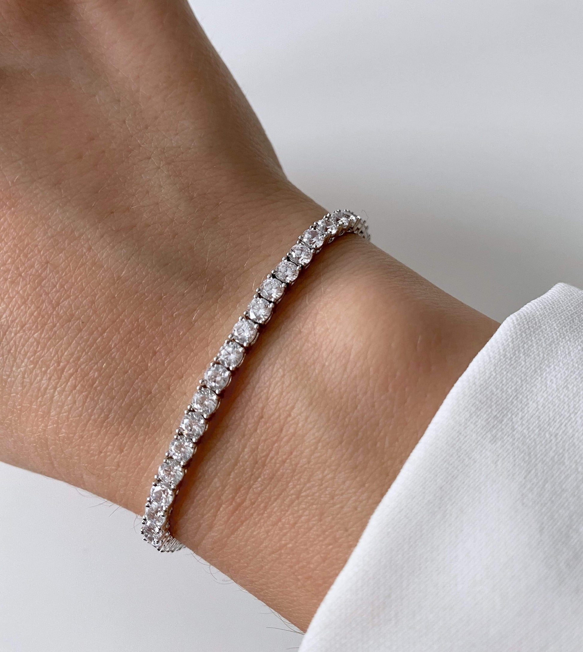 Close-up of a wrist adorned with a silver tennis bracelet featuring zirconia stones.