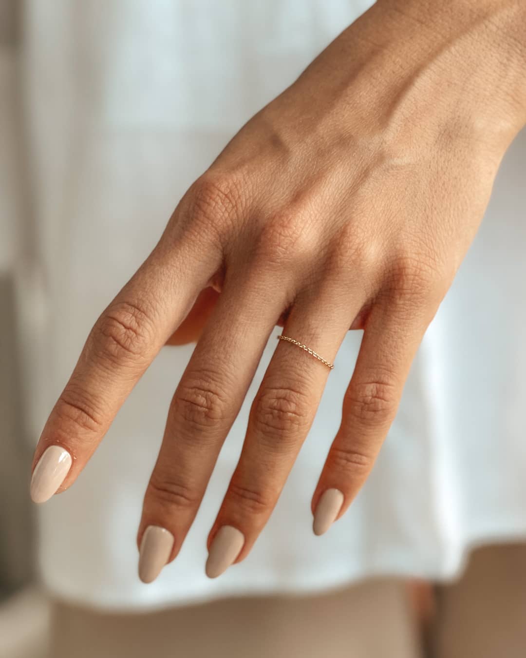 A delicate hand adorned with a 14K gold chain ring, showcasing nude manicured nails.