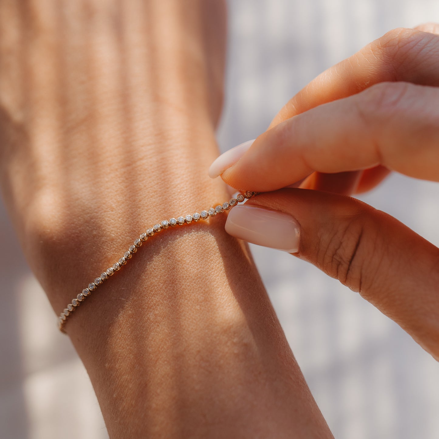 Close-up of a hand fastening a 14K yellow gold diamond tennis bracelet on the wrist in soft sunlight, showcasing luxurious, everyday elegance.