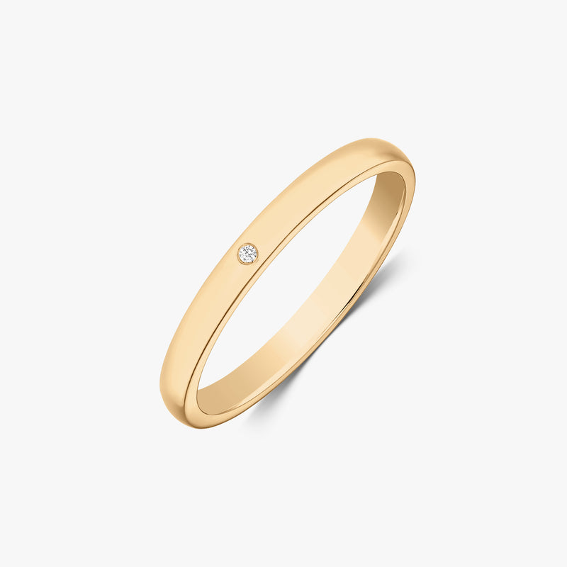 Slim 14k yellow gold wedding band featuring a flush-set petite round diamond, angled view on a white background.