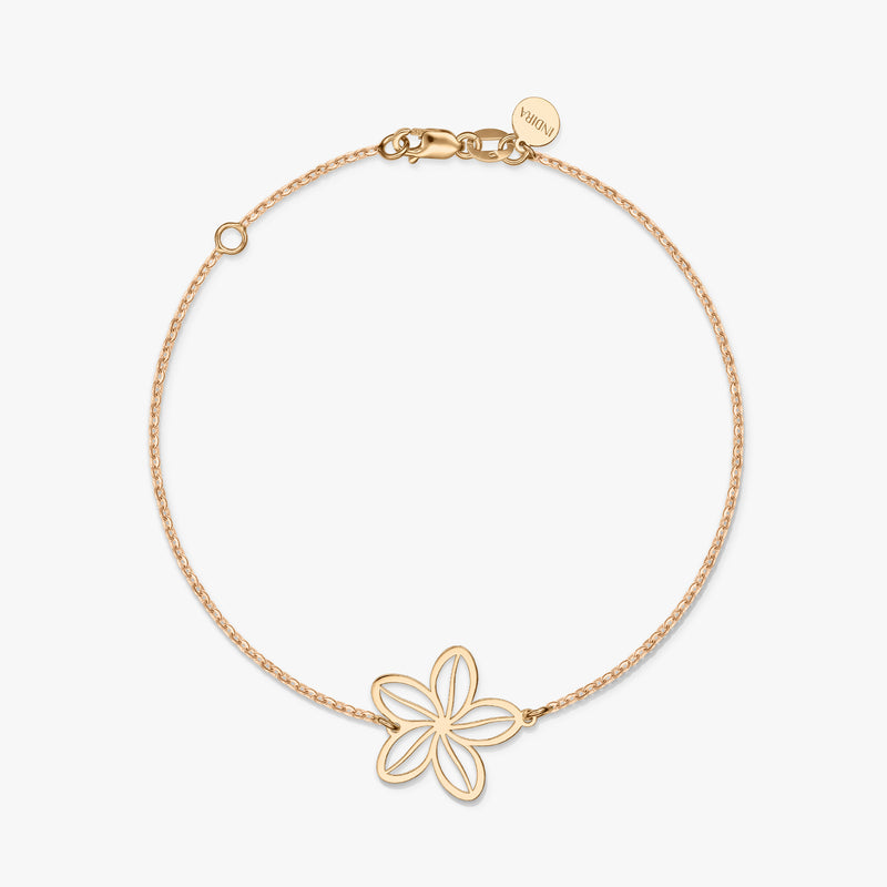 A minimalist gold bracelet with a delicate flower charm on a solid white background.