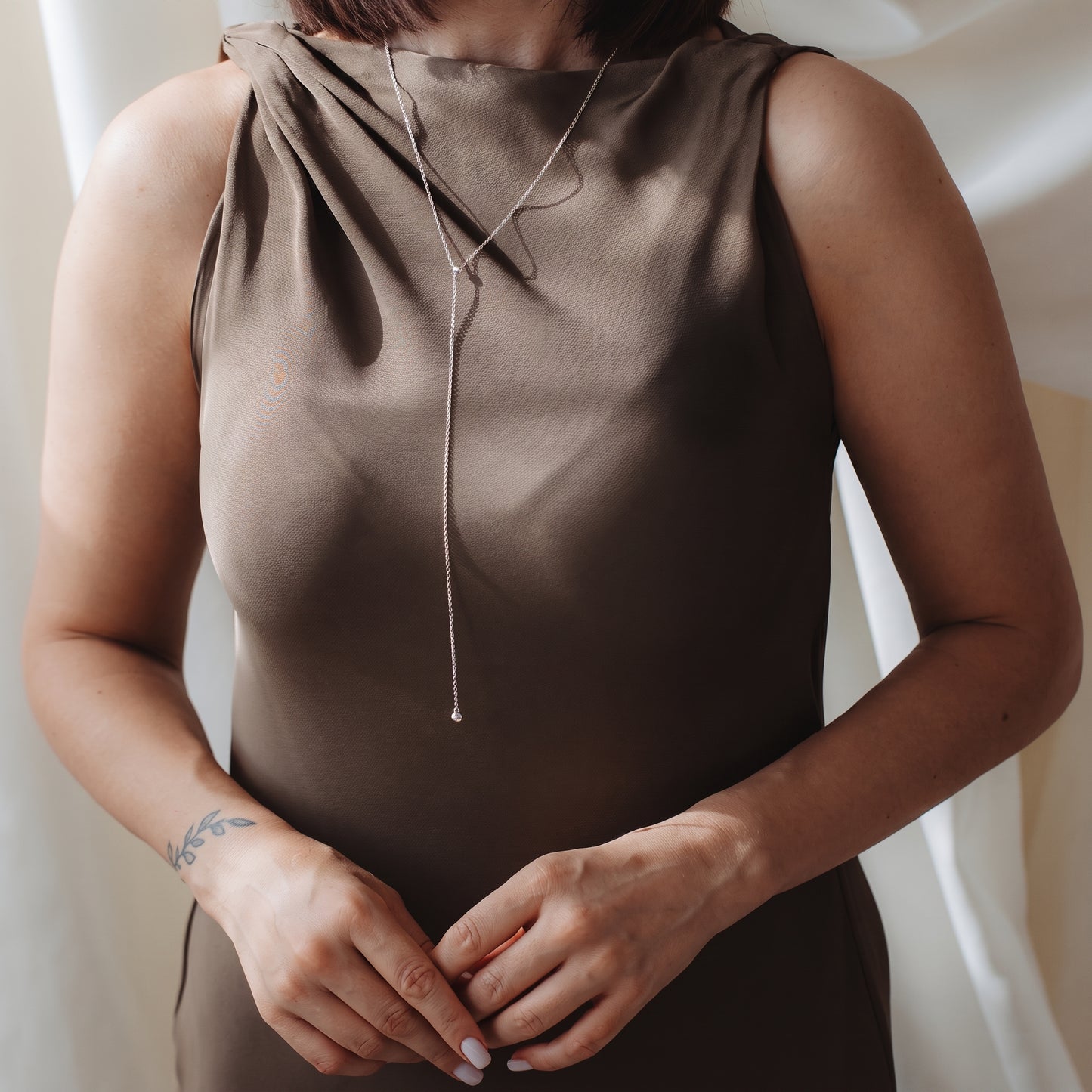 Close-up of a person wearing a sterling silver bola (lariat) necklace over a taupe satin dress in soft indoor light.