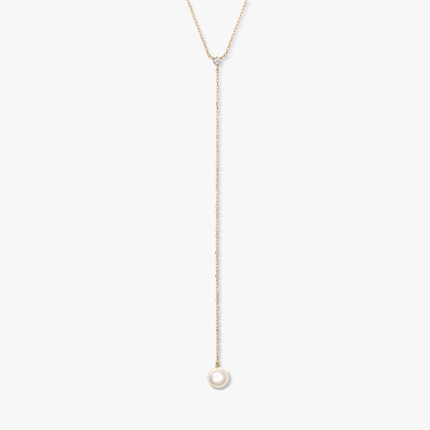 Minimalist gold lariat necklace featuring a single round white pearl drop and a delicate accent stone, centered on a white background.