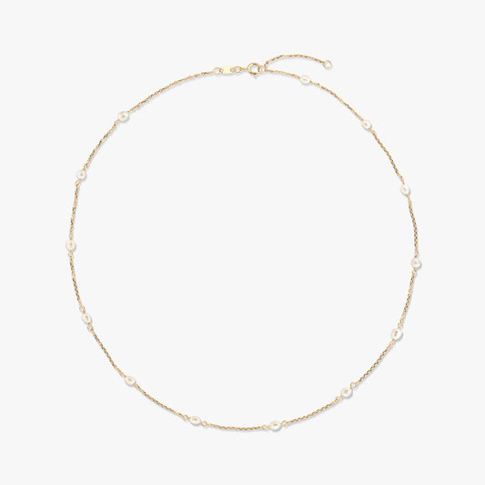 14K yellow gold station necklace with small natural white pearls spaced along a delicate chain, isolated on a white background.