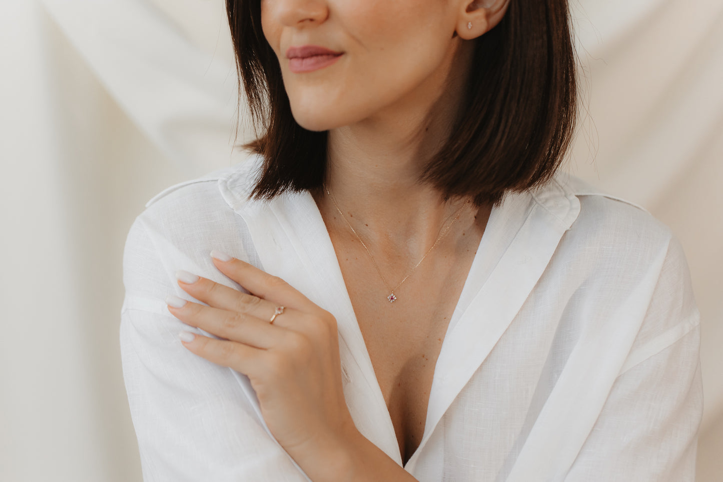 Close-up of a person in a white blouse wearing an elegant, delicate 14K yellow gold ring set with pink tourmaline and white sapphire; hand resting on the shoulder against a soft, neutral background.