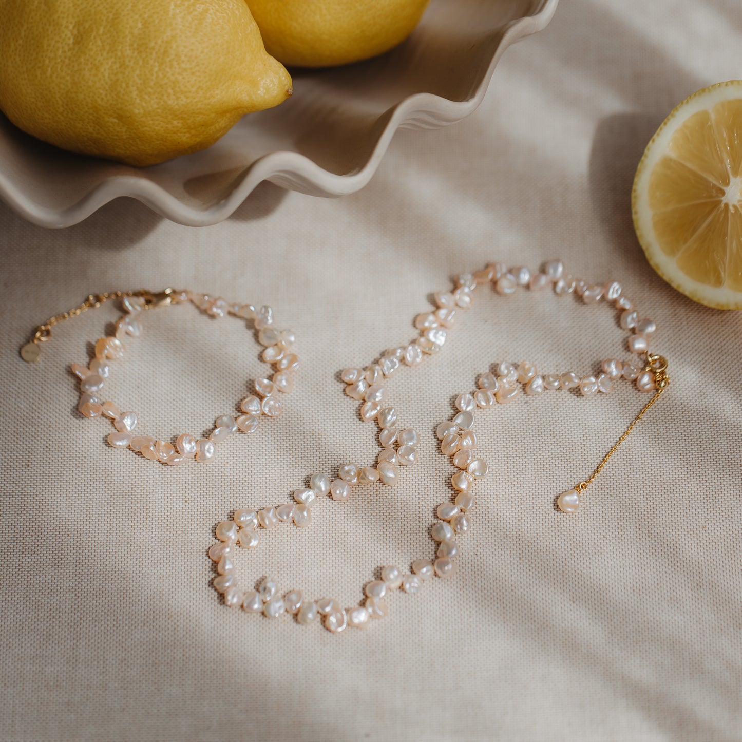 Gold-plated silver necklace with pink keshi pearls on neutral linen with lemons, with a matching bracelet nearby.