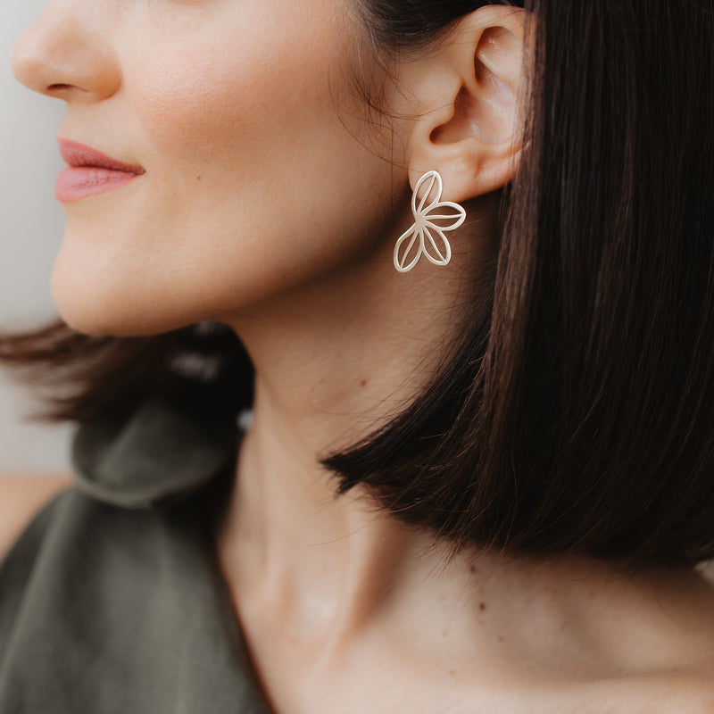 Close-up of a model wearing the Half Wildflower 14K yellow gold stud earring with an open-petal design, in soft indoor light against a neutral background.