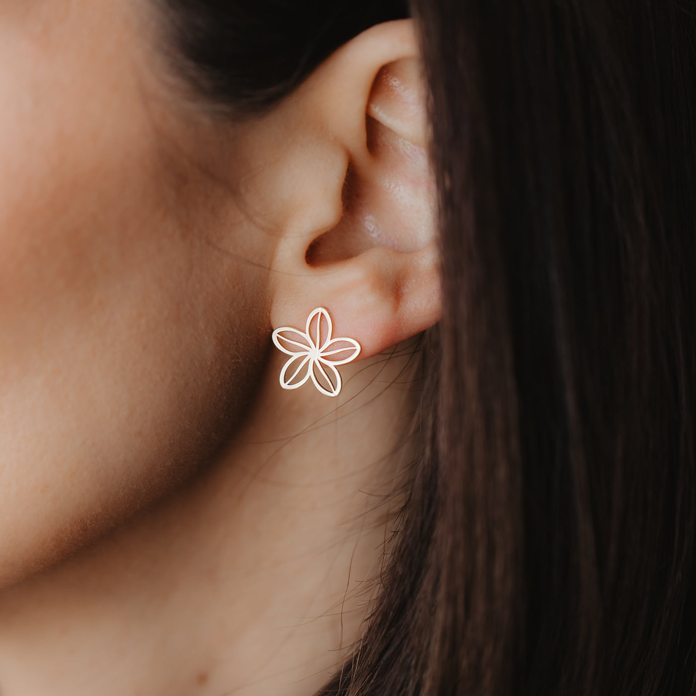 Close-up of an ear with a delicate 14K yellow gold openwork flower stud earring.