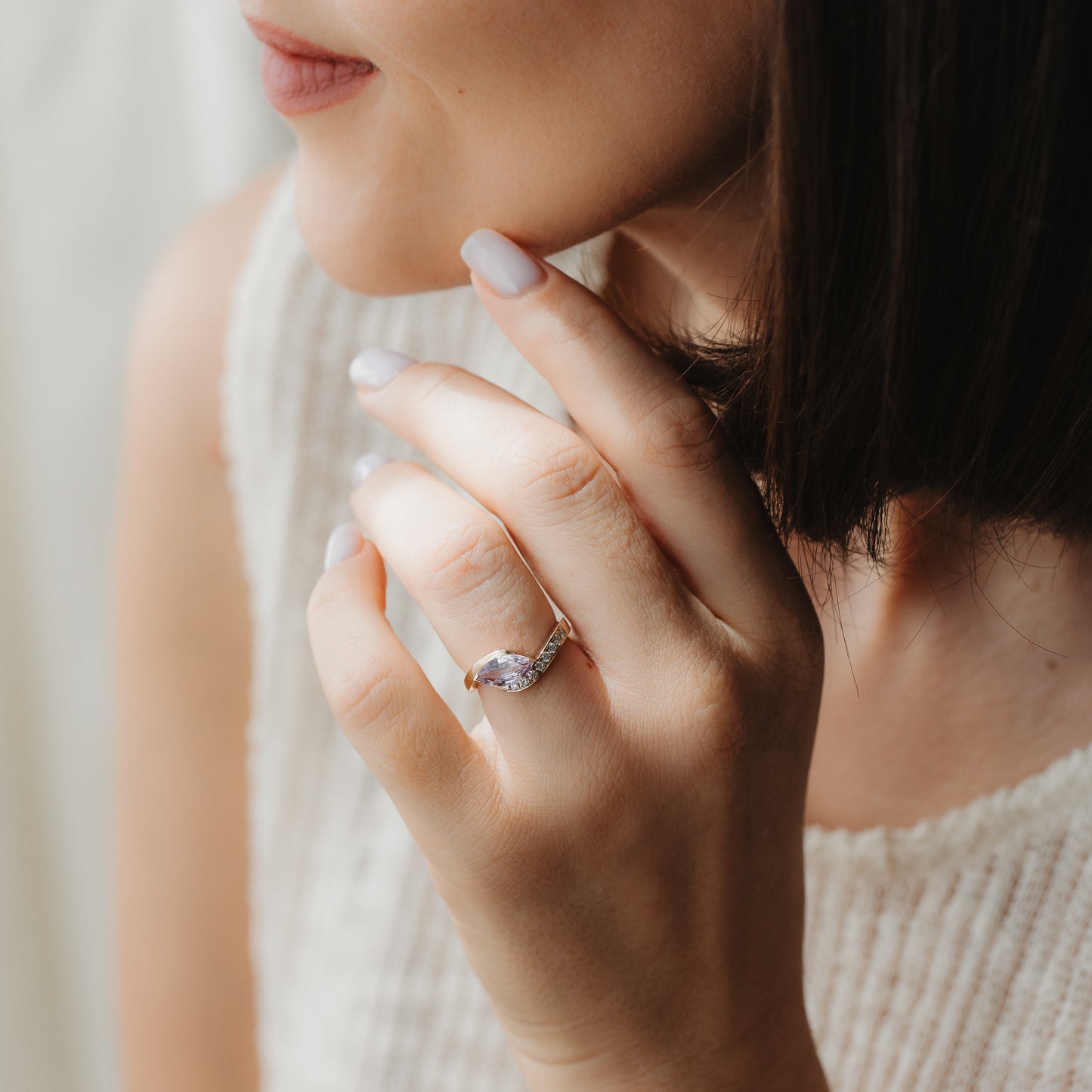 Close-up of a hand wearing a 14k yellow gold marquise sapphire and diamond engagement ring, shown near the face in soft natural light.