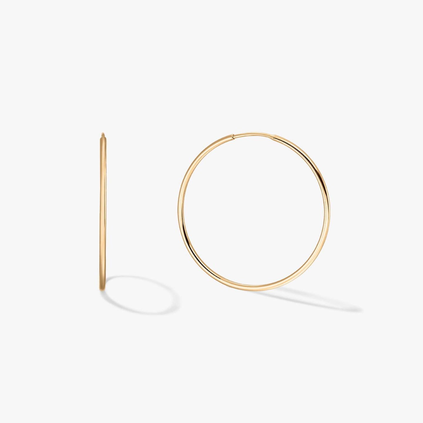 Pair of large, thin 14K yellow gold hoop earrings on a white background, one front-facing and one in profile with soft shadows.