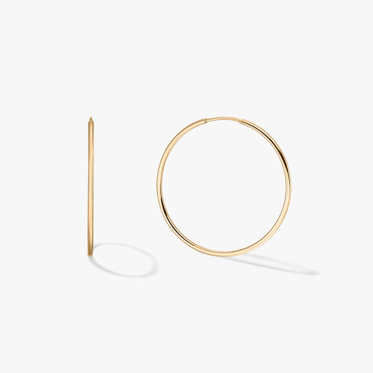 Pair of large, thin 14K yellow gold hoop earrings on a white background, one front-facing and one in profile with soft shadows.