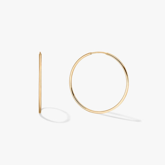Pair of large, thin 14K yellow gold hoop earrings on a white background, one front-facing and one in profile with soft shadows.