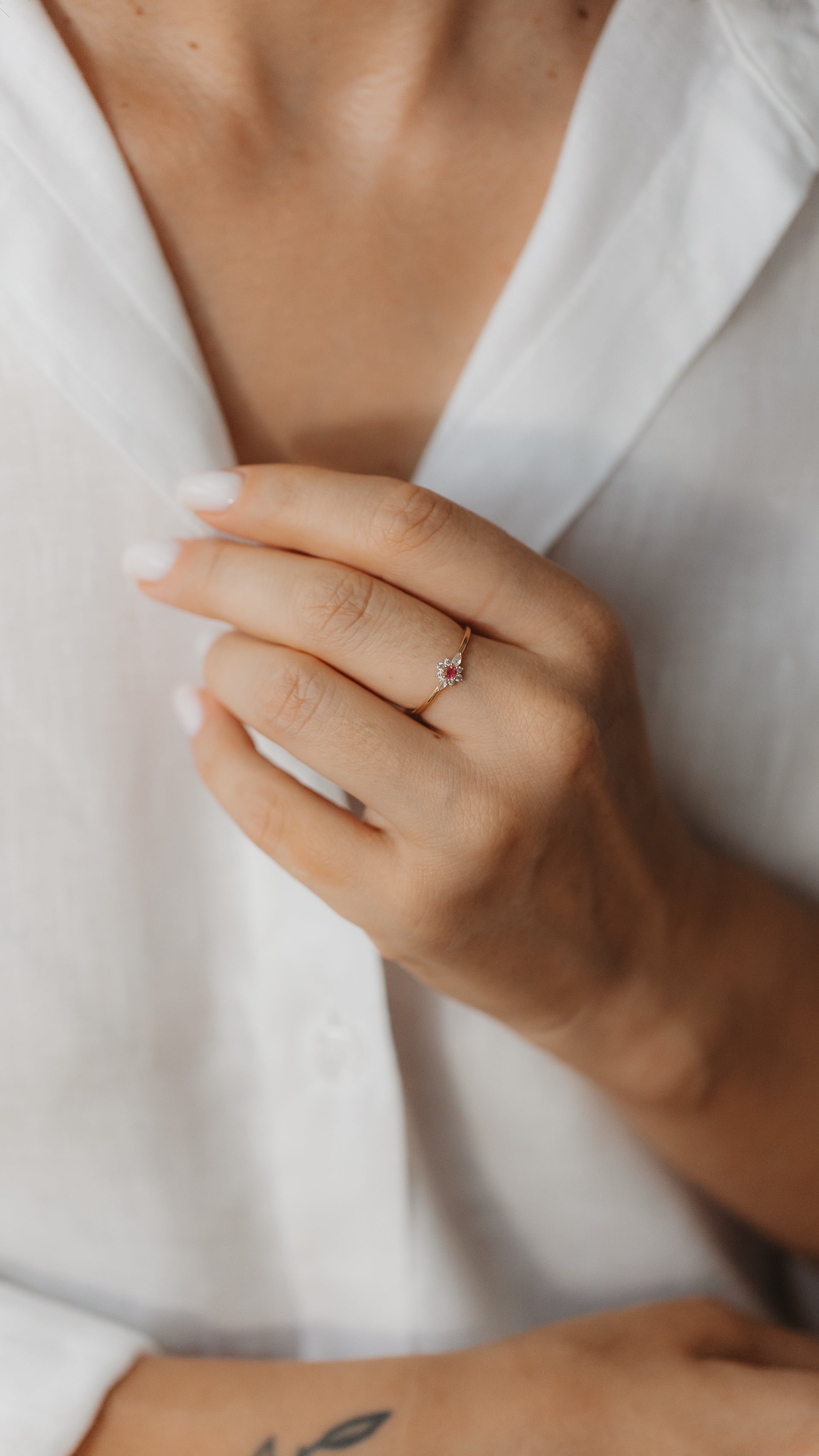 Close-up of a hand wearing a delicate yellow gold ring featuring a pink tourmaline center surrounded by a halo of white sapphires.