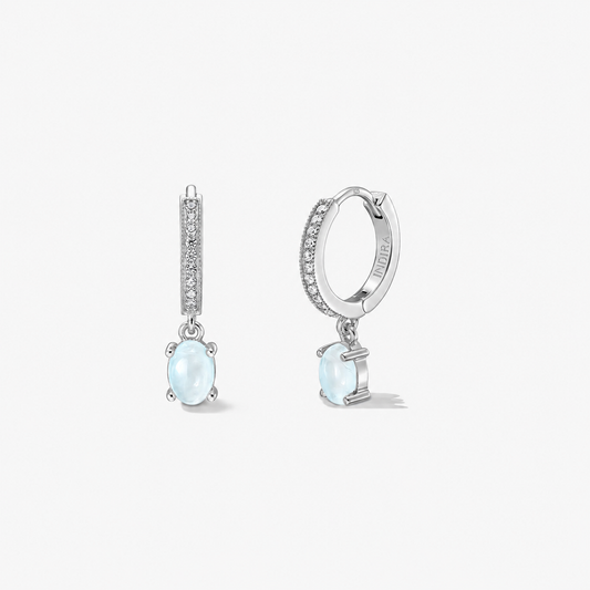 Sterling silver huggie earrings with pavé hoops and oval milky-blue moonstone drops, photographed on a white background from front and side views.