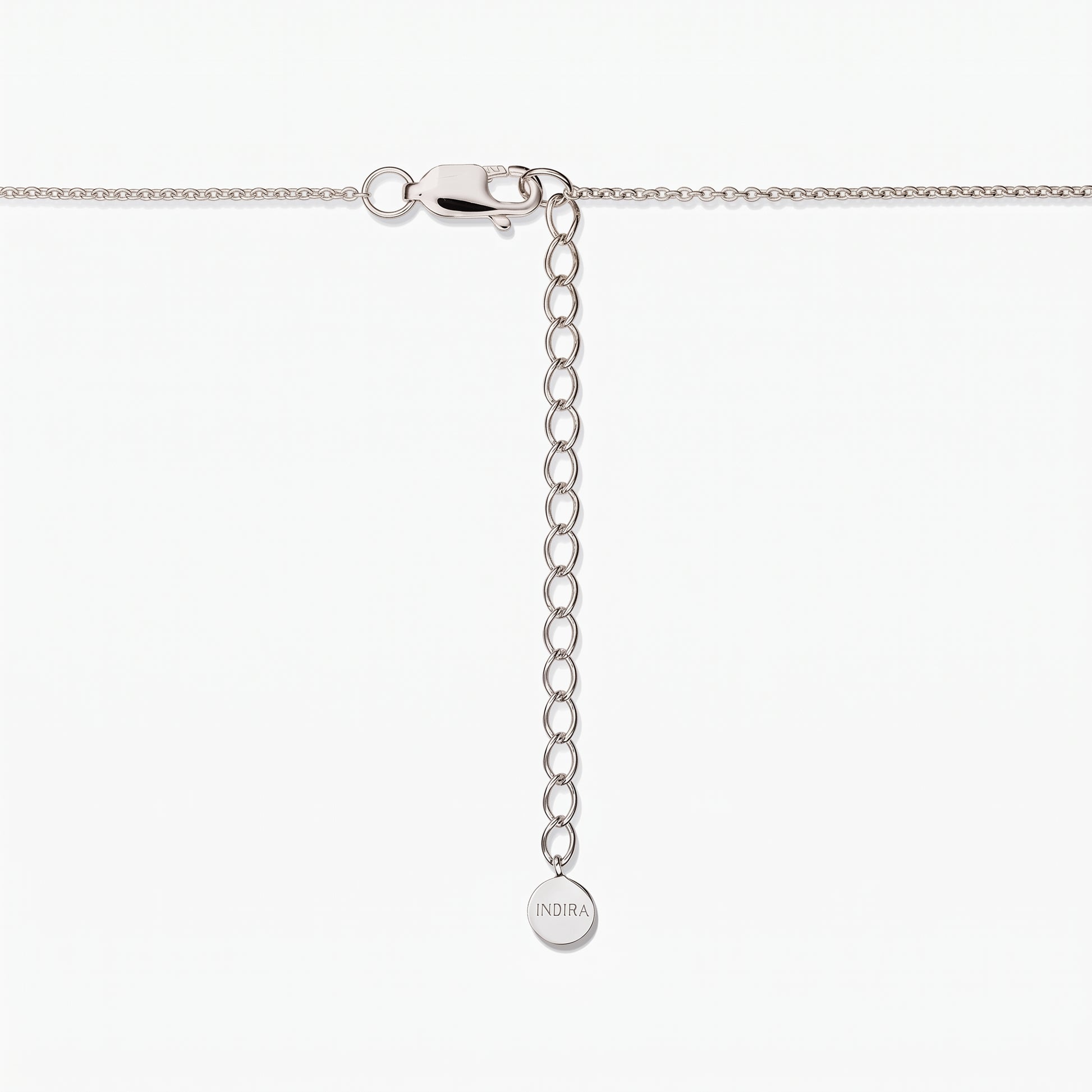 Close-up of a sterling silver necklace clasp with an adjustable extender chain and a small round tag engraved “INDIRA,” against a white background.