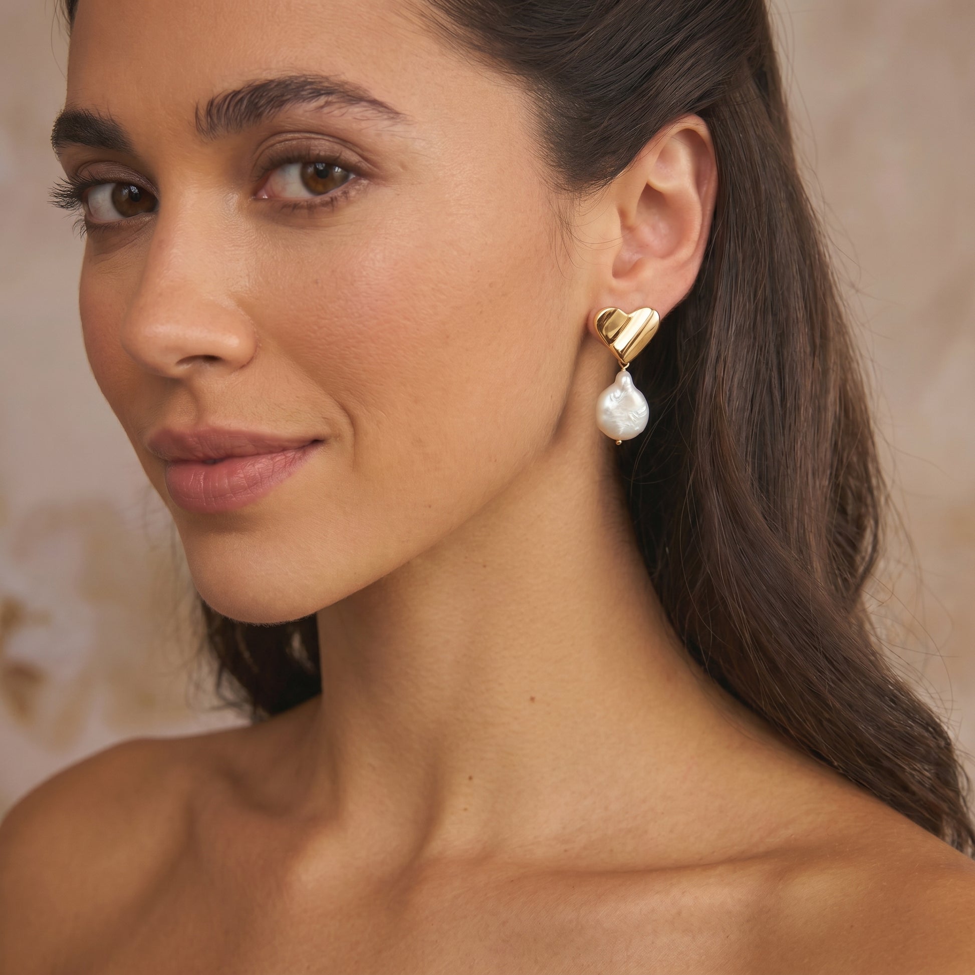 Close-up of a woman wearing a gold-plated silver earring featuring a heart shape and a dangling natural pear-shaped stone.
