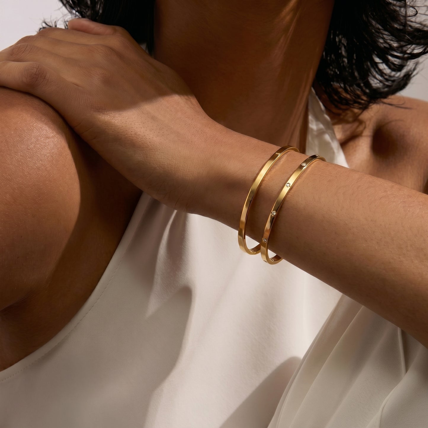 Close-up of a person's arm showcasing two gold bangle bracelets on a white background.