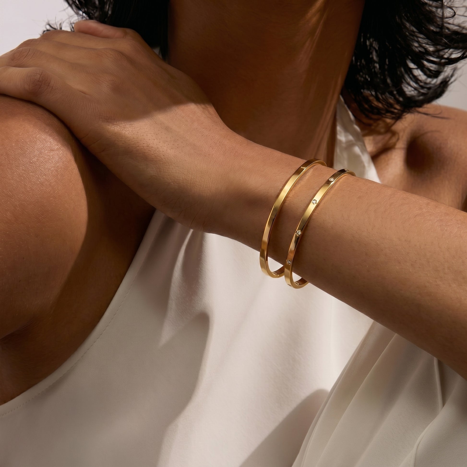 Close-up of a person's arm showcasing two gold bangle bracelets on a white background.