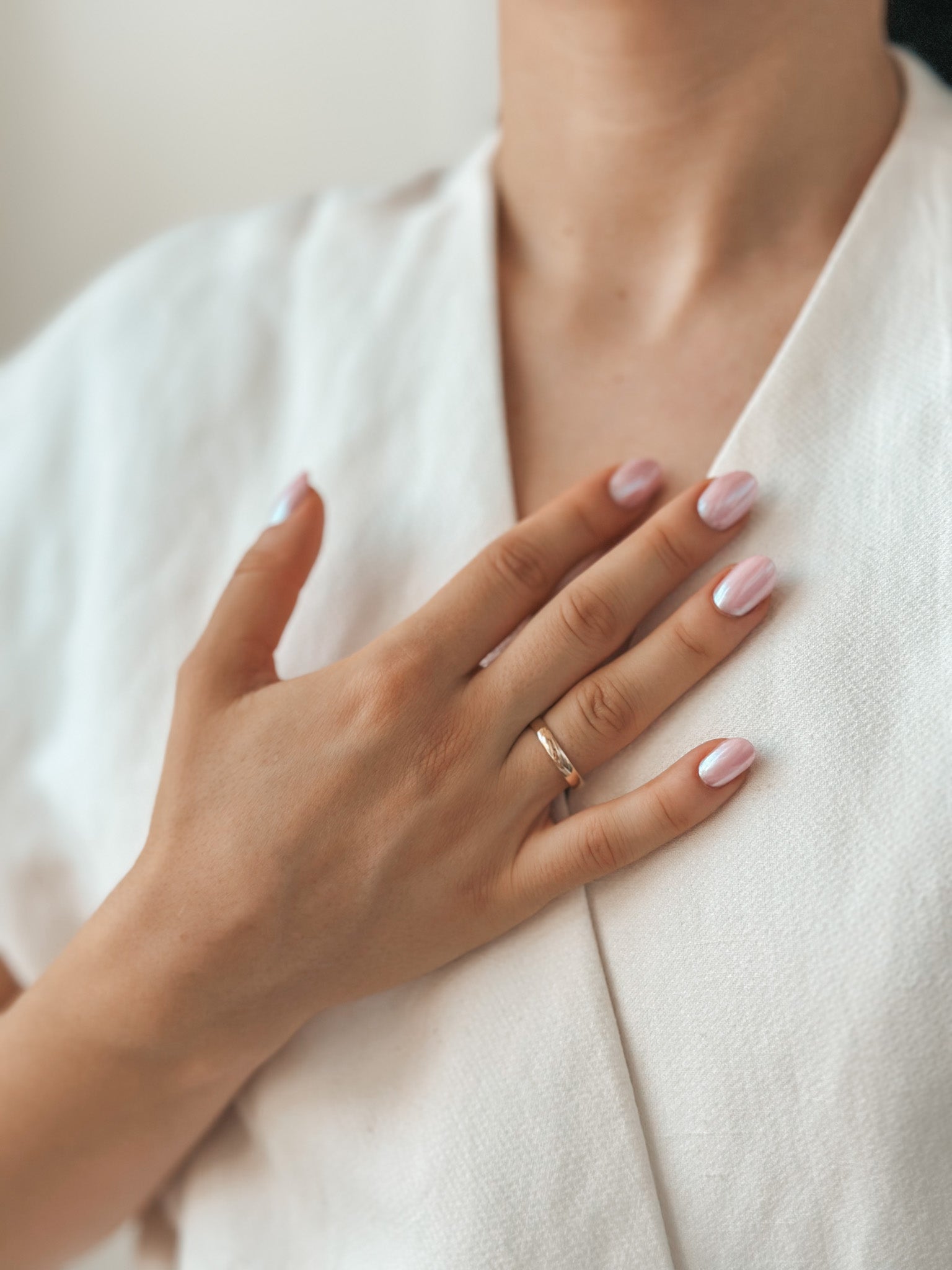 Close-up of a hand wearing a gold wedding band and manicured nails on white fabric.