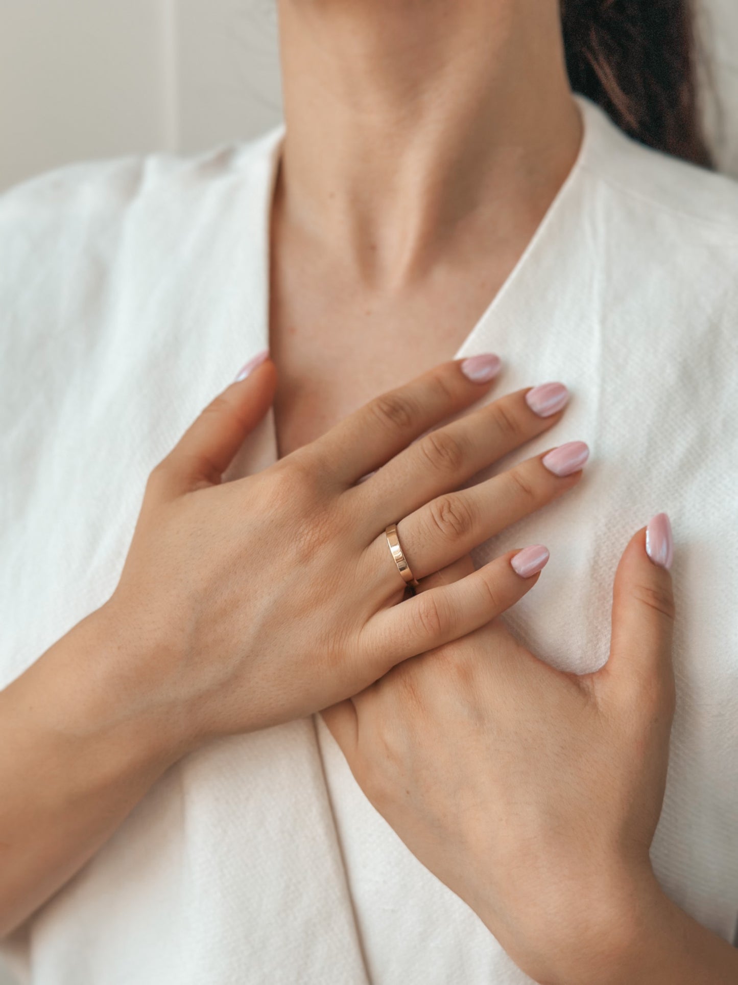 Close-up image of hands featuring a simple gold wedding band on the ring finger, set against a white cloth background.