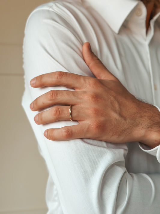 Close-up of a hand wearing a gold wedding ring against a white shirt sleeve.