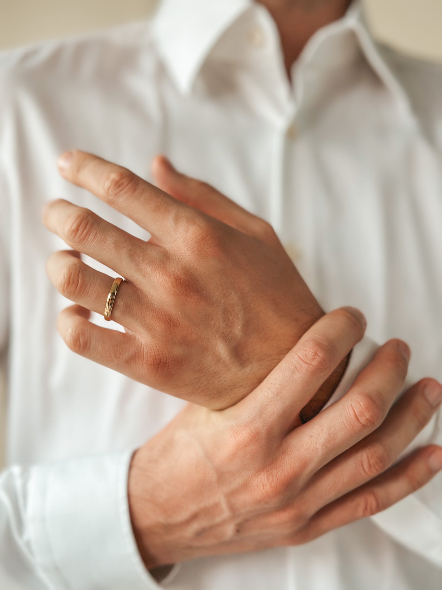 Close-up of hands displaying a gold wedding band on the ring finger, wearing a white shirt.