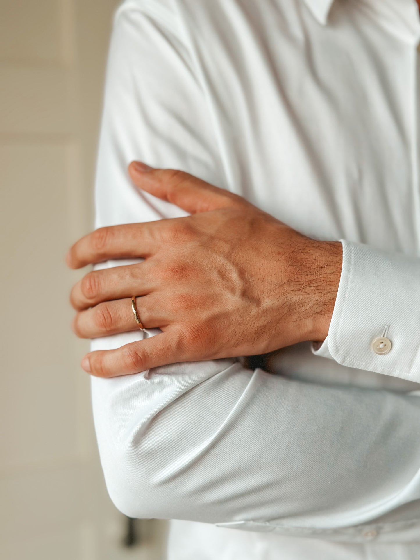 Close-up of a person wearing a white shirt and a slim gold wedding band on their finger.