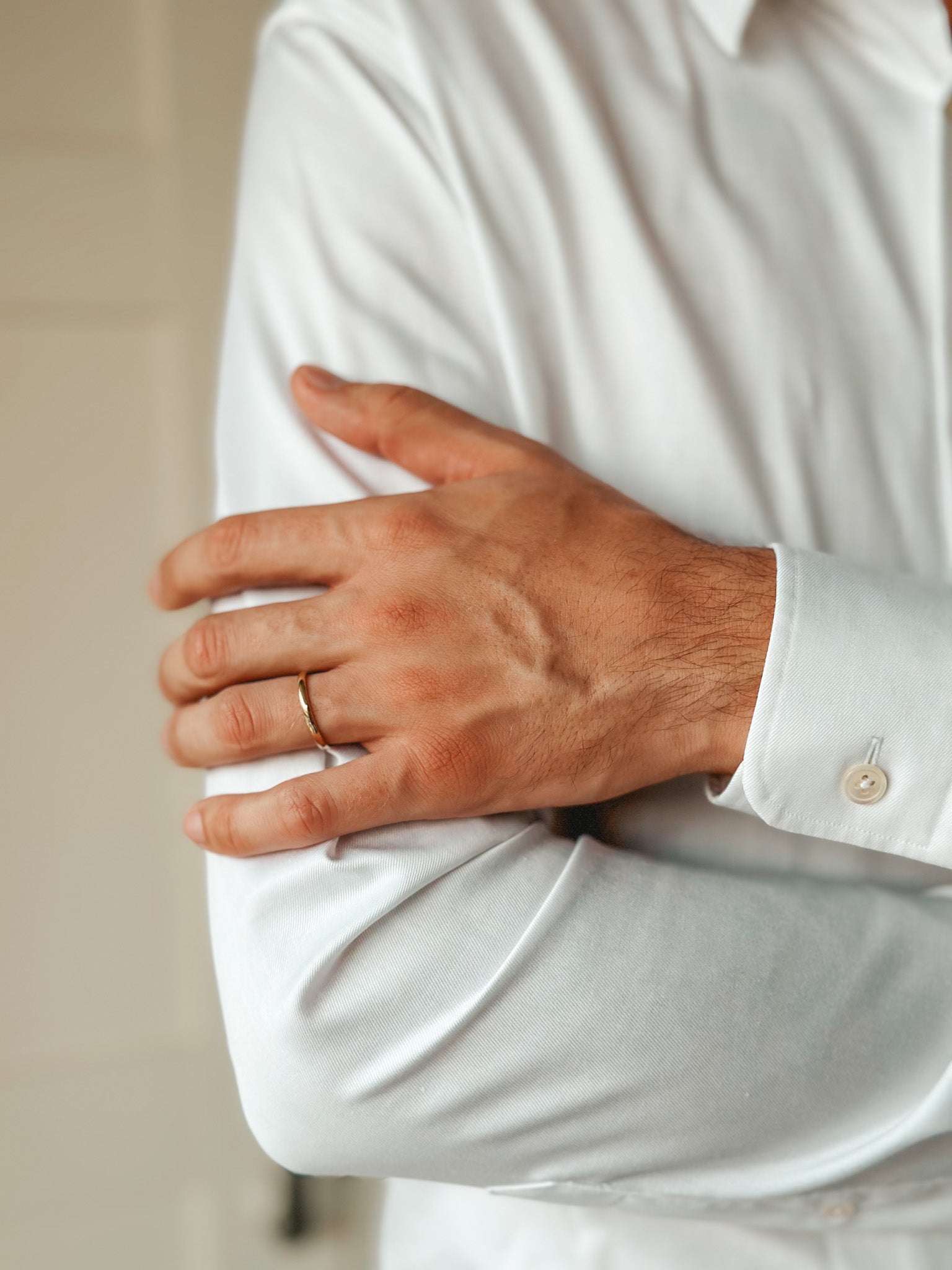 Close-up of a person wearing a white shirt and a slim gold wedding band on their finger.