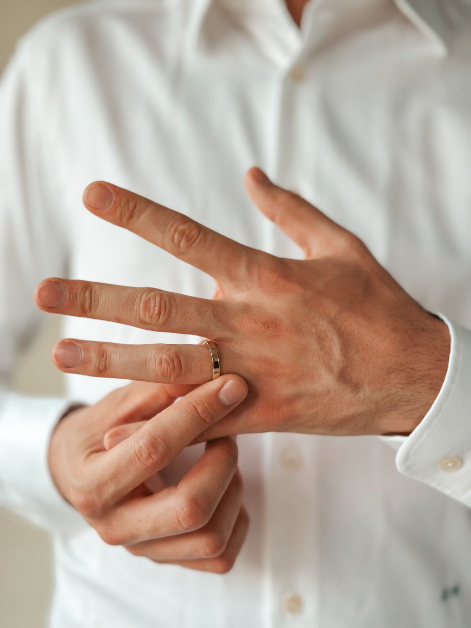 A person wearing a white shirt, slipping on a simple gold wedding band.