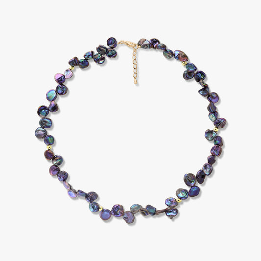 Iridescent black keshi pearl necklace with small gold accents and an adjustable extender chain, photographed on a white background.