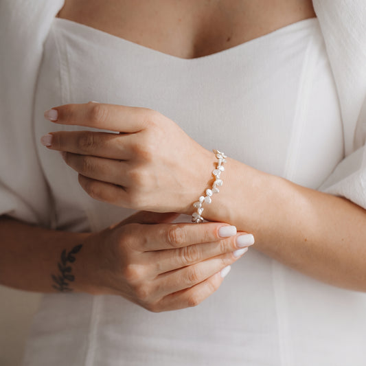 Close-up of hands wearing a gold-plated sterling silver bracelet with white keshi pearls against a white dress.